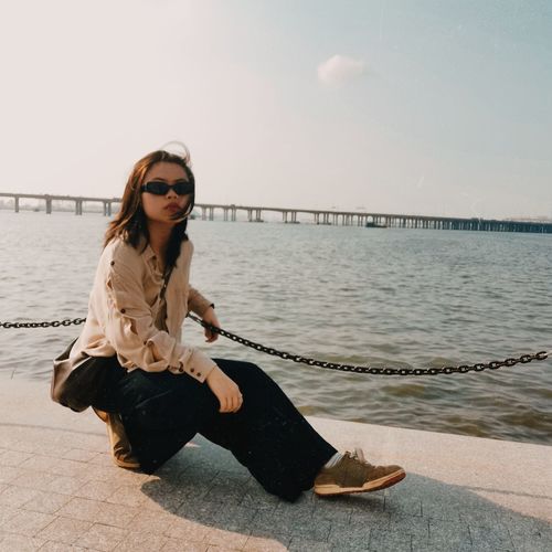 A young woman fighting depression, wearing sunglasses, facing sky and sea breeze.