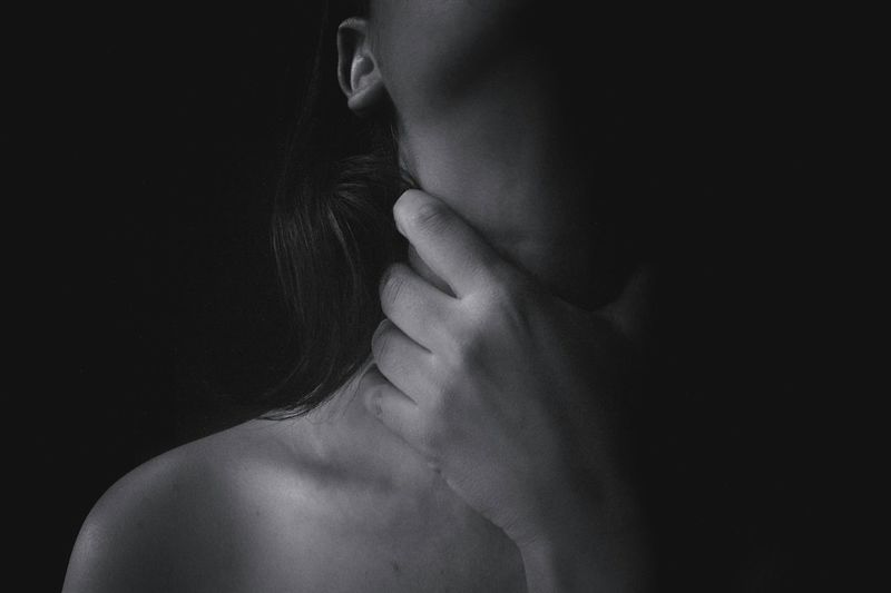 Midsection of topless woman choking throat against black background.