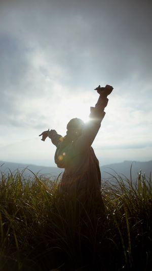 Side view of woman with arms raised standing against sky