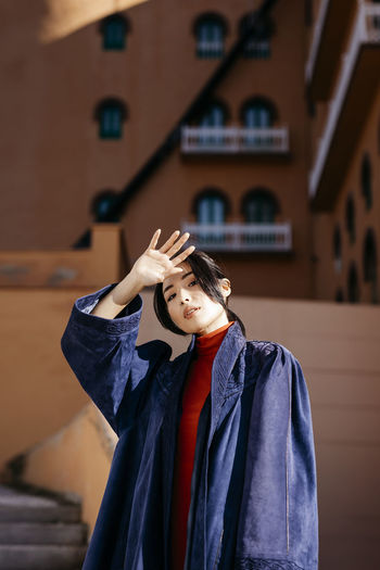Young woman shielding eyes while standing in front of building during sunny day