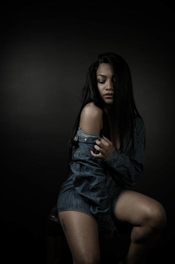 Young woman sitting against black background