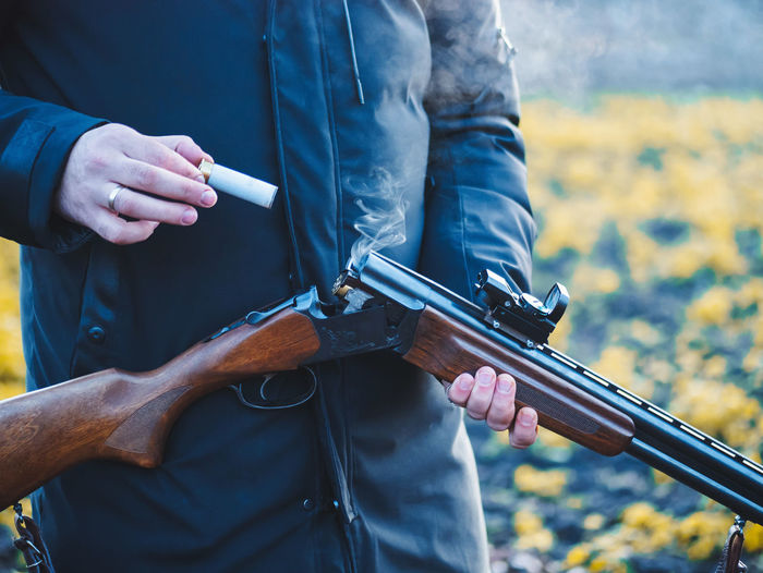 Midsection of man removing bullet from shotgun while standing outdoors