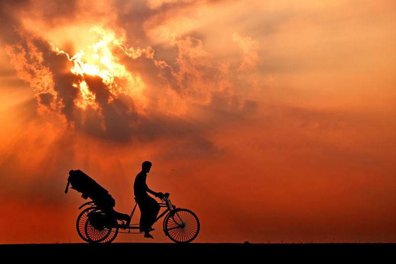 Silhouette man riding bicycle against orange sky. silhouette of a man and rickshaw in bangladesh. 