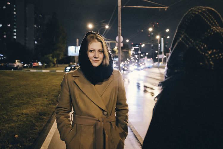 Portrait of woman standing on illuminated street in city at night
