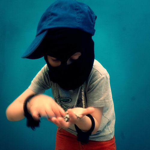 Boy looking at pendant while wearing black mask against blue wall