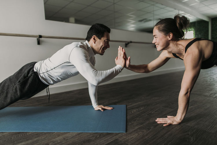 Male and female friends high five while doing pushups at gym