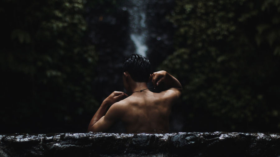 Back view of a man soaking under a waterfall 