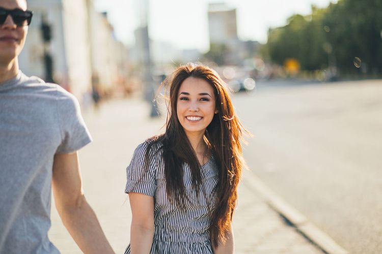 Portrait of smiling young woman standing with man on sidewalk