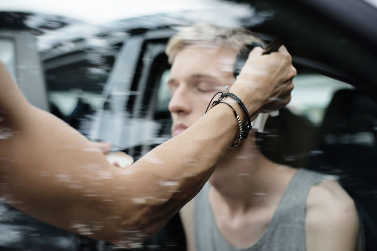 Cropped hand applying make-up on male friend seen through car window