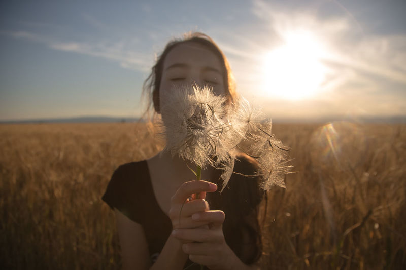 Young woman blowing dandelion on field against sky