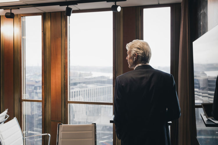 Rear view of senior male entrepreneur standing by reflection on television in board room