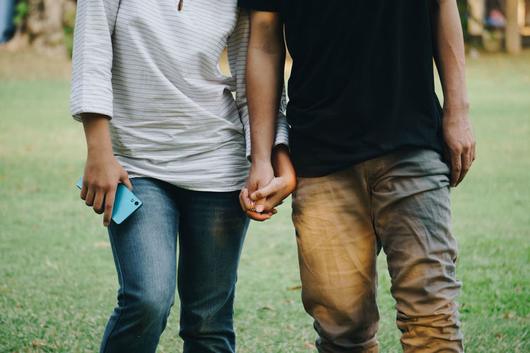 Midsection of couple holding hands while standing in park