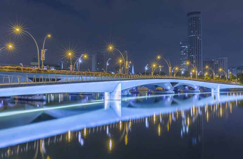 Illuminated bridge over water in city at night