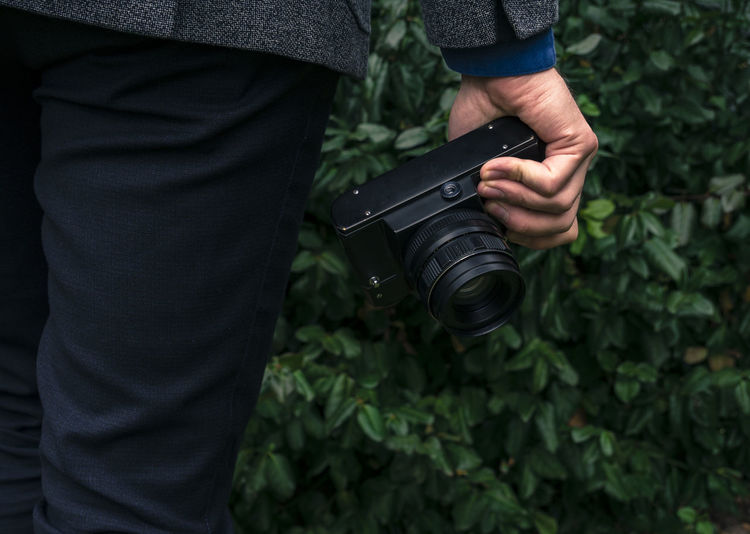 Midsection of man holding camera while standing by plant