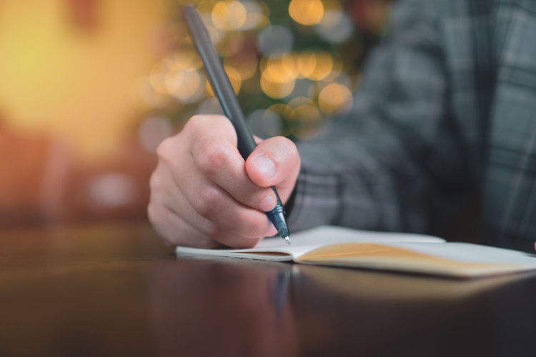 Midsection of man holding pen over book on table