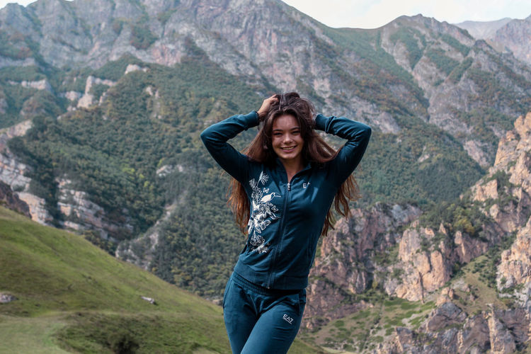 Portrait of smiling young woman standing against mountain range