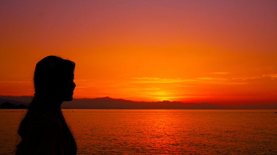Silhouette woman by sea against sky during sunset