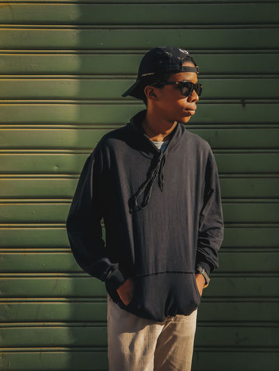 Young man wearing sunglasses standing against wall