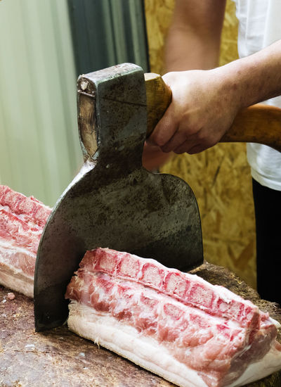 Midsection of butcher cutting meat in shop
