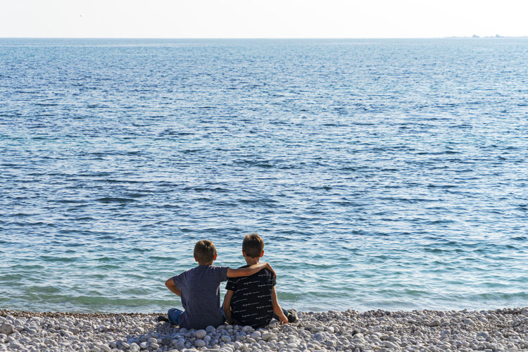 Rear view of couple sitting on shore against sea