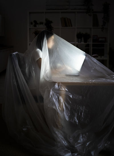 Young woman using laptop at table while covered in plastic during covid-19