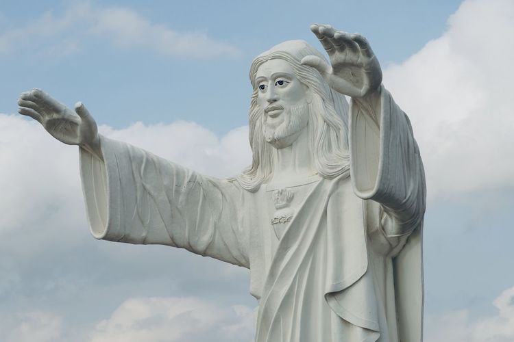 Standing majestic jesus statue blessing with both the hands against blue sky background.