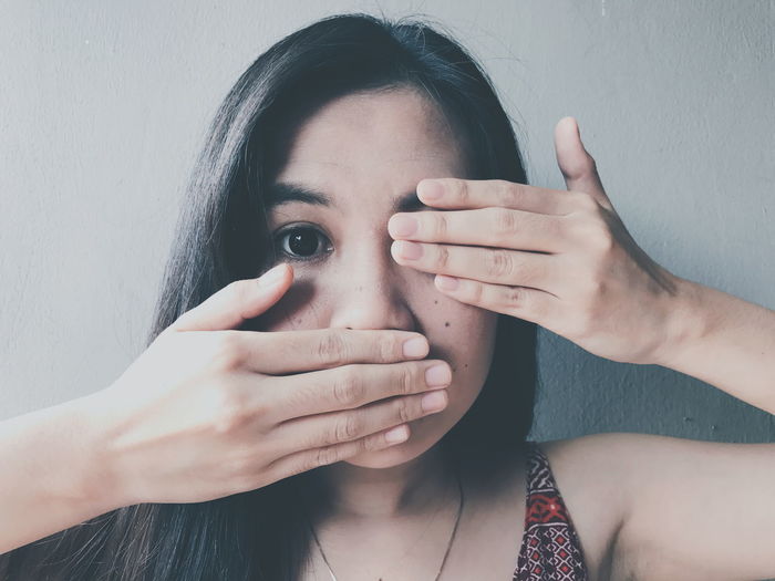 Close-up portrait of young woman covering face with hands