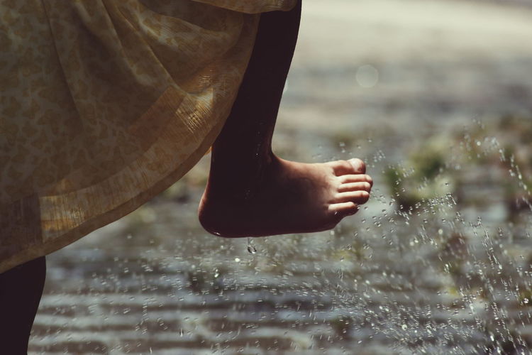 Low section of girl standing by sprinkler on footpath