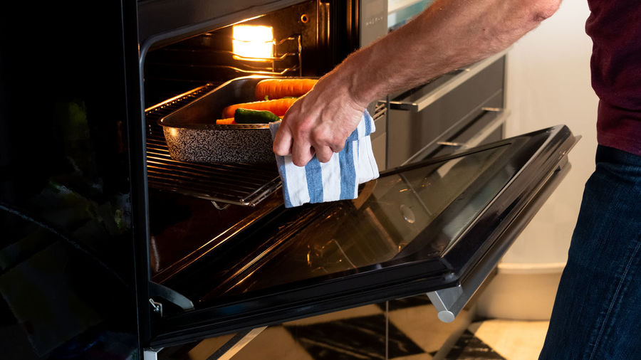 Man putting baking tray with vegetables into oven to roast. healthy