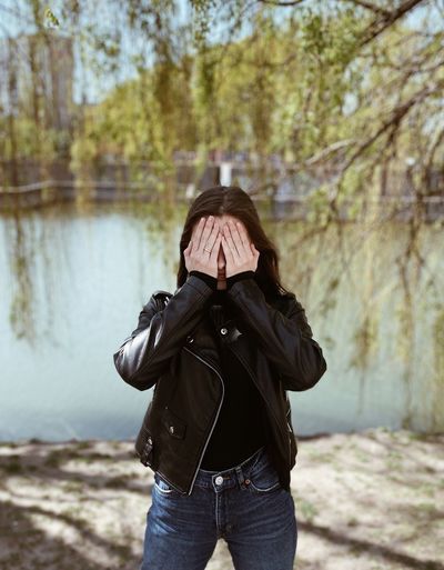 Woman covering face standing by lake