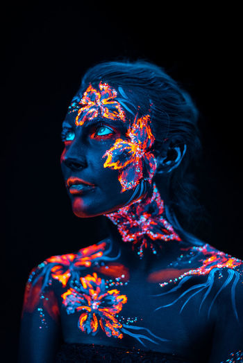 Close-up of woman with illuminated body paint against black background