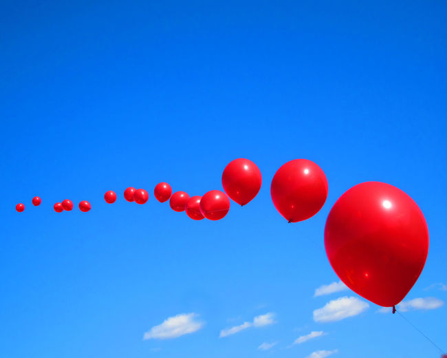 Low angle view of red balloons against blue sky on sunny day