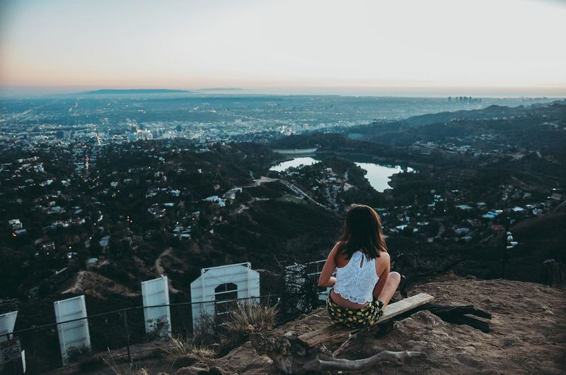 Woman sitting on mountain against clear sky