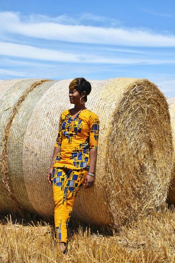 Full length of smiling woman standing by hay bale on field