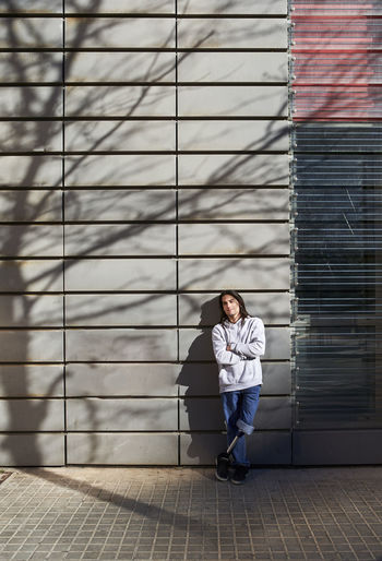 Young disabled man with arms crossed standing against wall with tree shadow