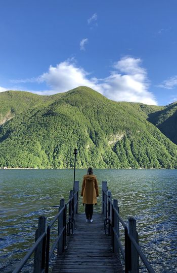 Rear view of woman standing on pier over lake against mountains