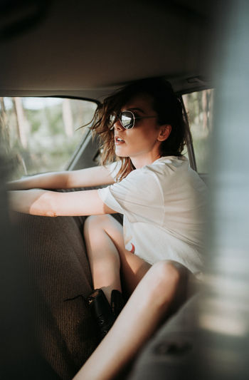 Hipster woman with sunglasses in the back seat of a car.
