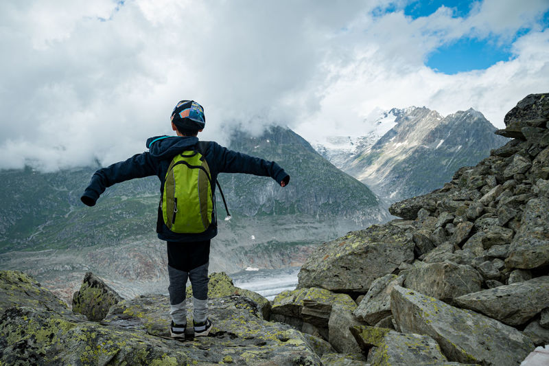 Rear view of one boy standing on rocks and enjoying view of nature. aletsch glacier, switzerland.