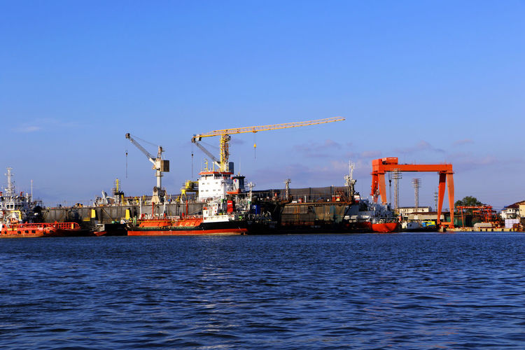Cranes at commercial dock by sea against sky