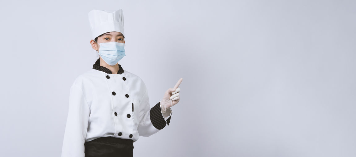 Portrait of chef wearing flu mask standing against white background