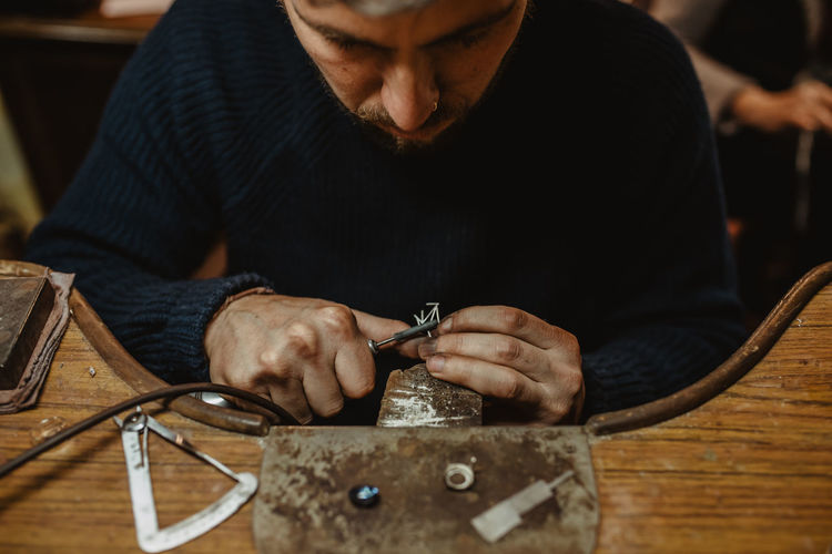 Jeweler using professional polishing machine on workbench while making metal ring in workshop