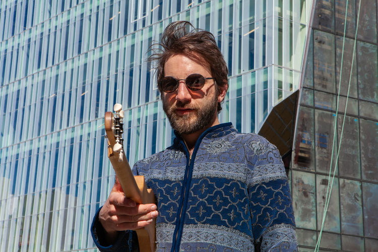 Portrait of man wearing sunglasses holding guitar while standing outdoors