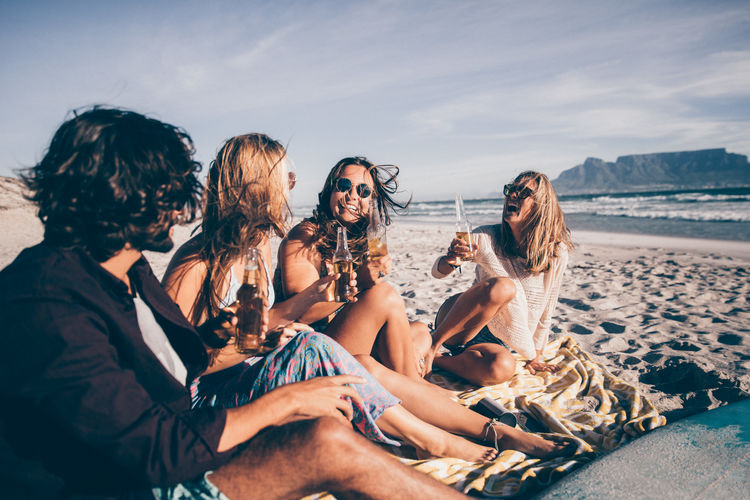 Man and women holding beer bottles while sitting at beach