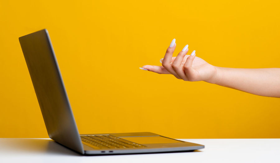Cropped hands using laptop against yellow background