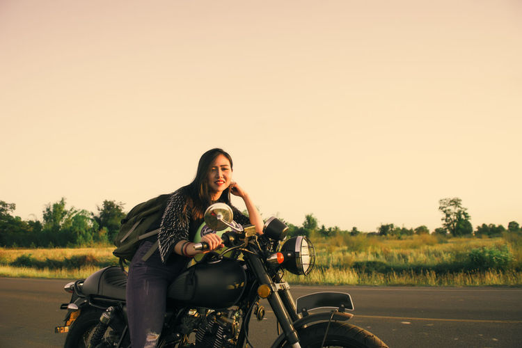 Portrait of young woman sitting on motorcycle against clear sky