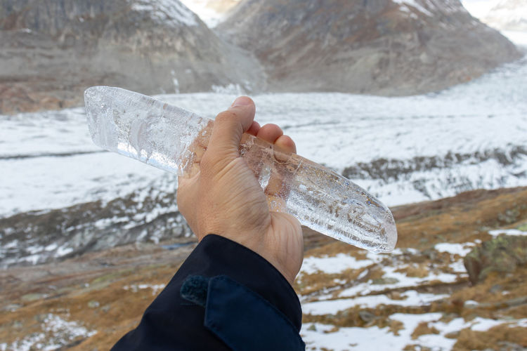 Close up of icicle held in front of glacier and mountain landscape at the aletsch glacier.