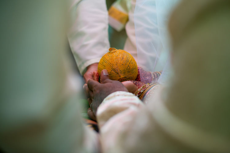 Cropped hands of people holding ring over coconut during wedding