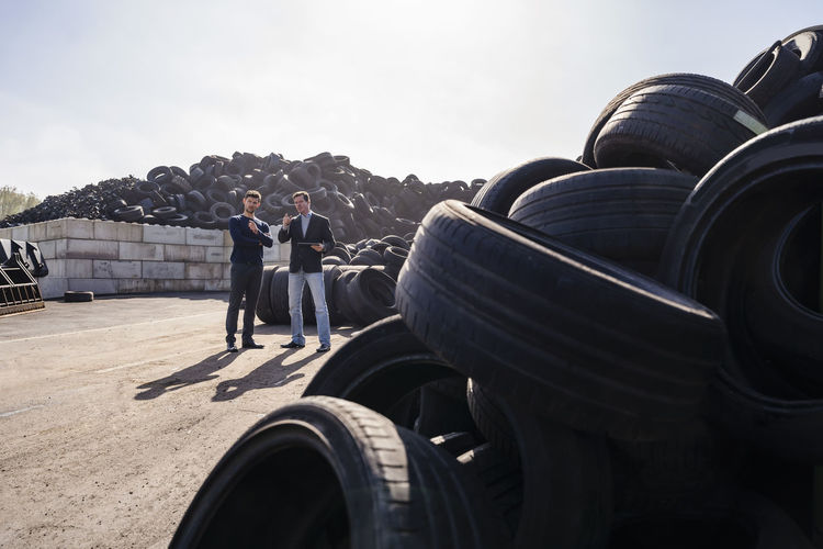 Businessmen discussing over heap of rubber tires at recycling plant