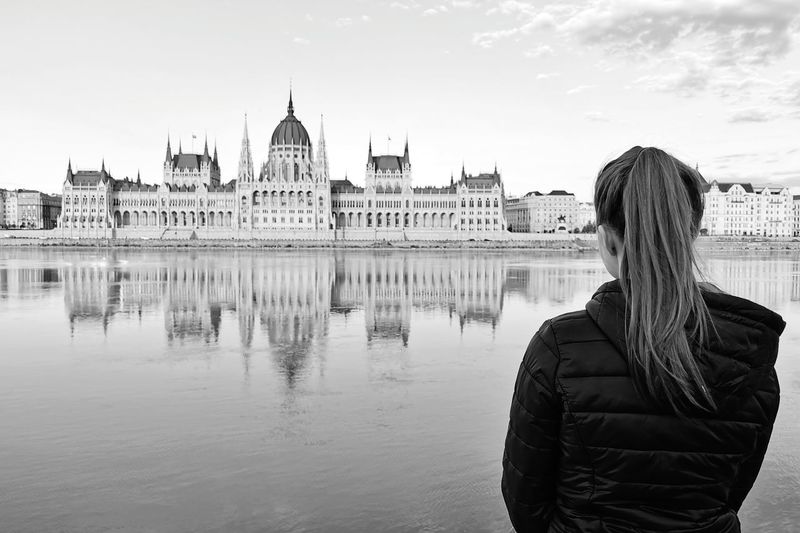 Rear view of woman standing by danube river in front of the parlament