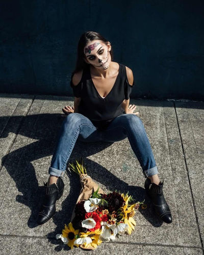 Portrait of woman with spooky halloween make-up sitting by bouquet on footpath